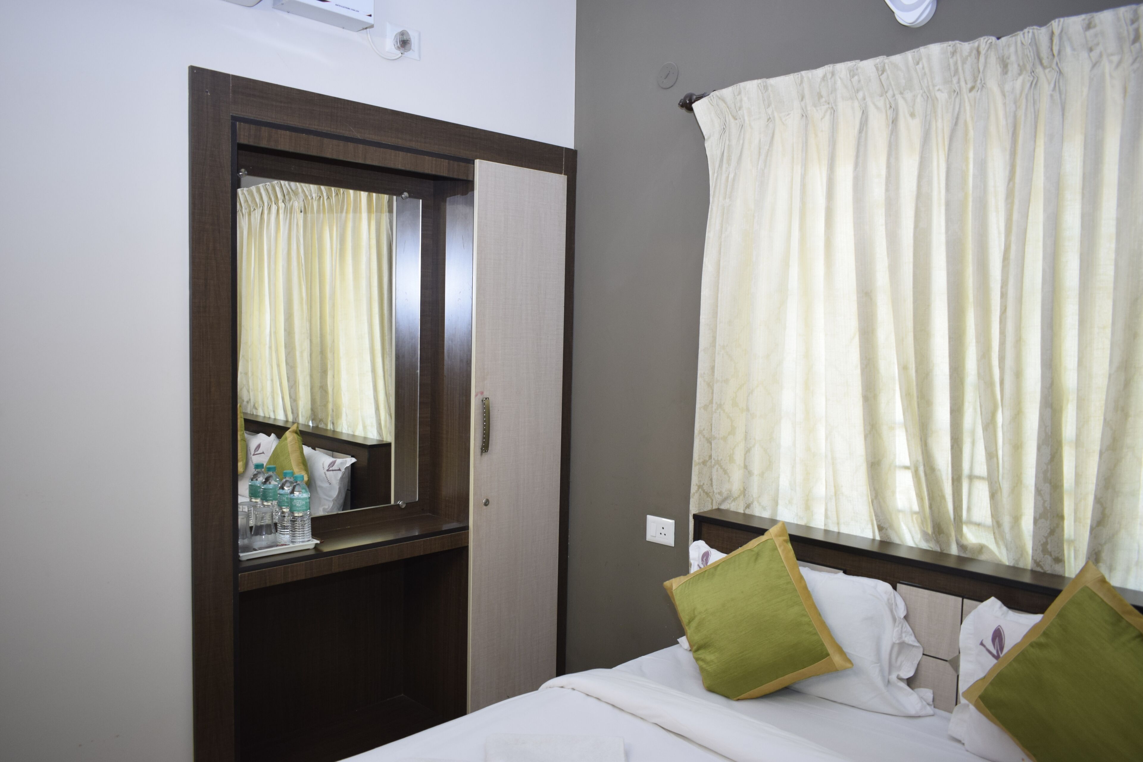 Una habitación de hotel con cama, espejo, ventana con cortinas y un armario de madera.