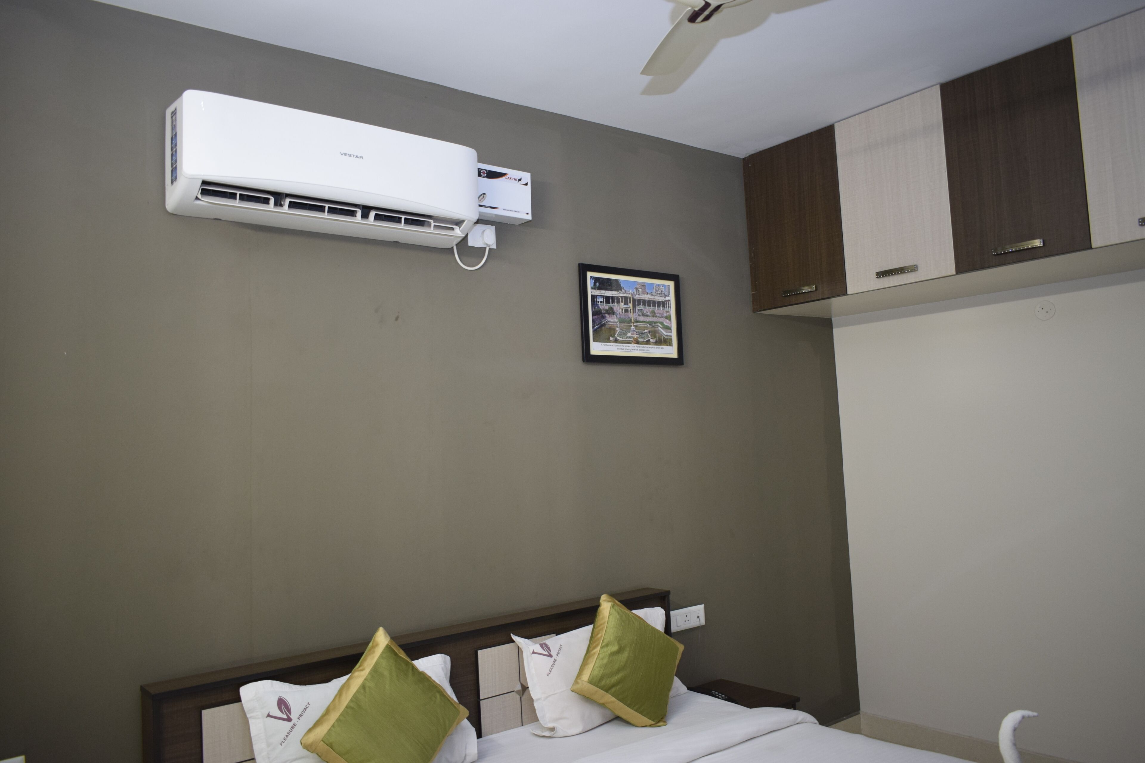 Una habitación de hotel con una cama, ventilador de techo, aire acondicionado y un cuadro en la pared.