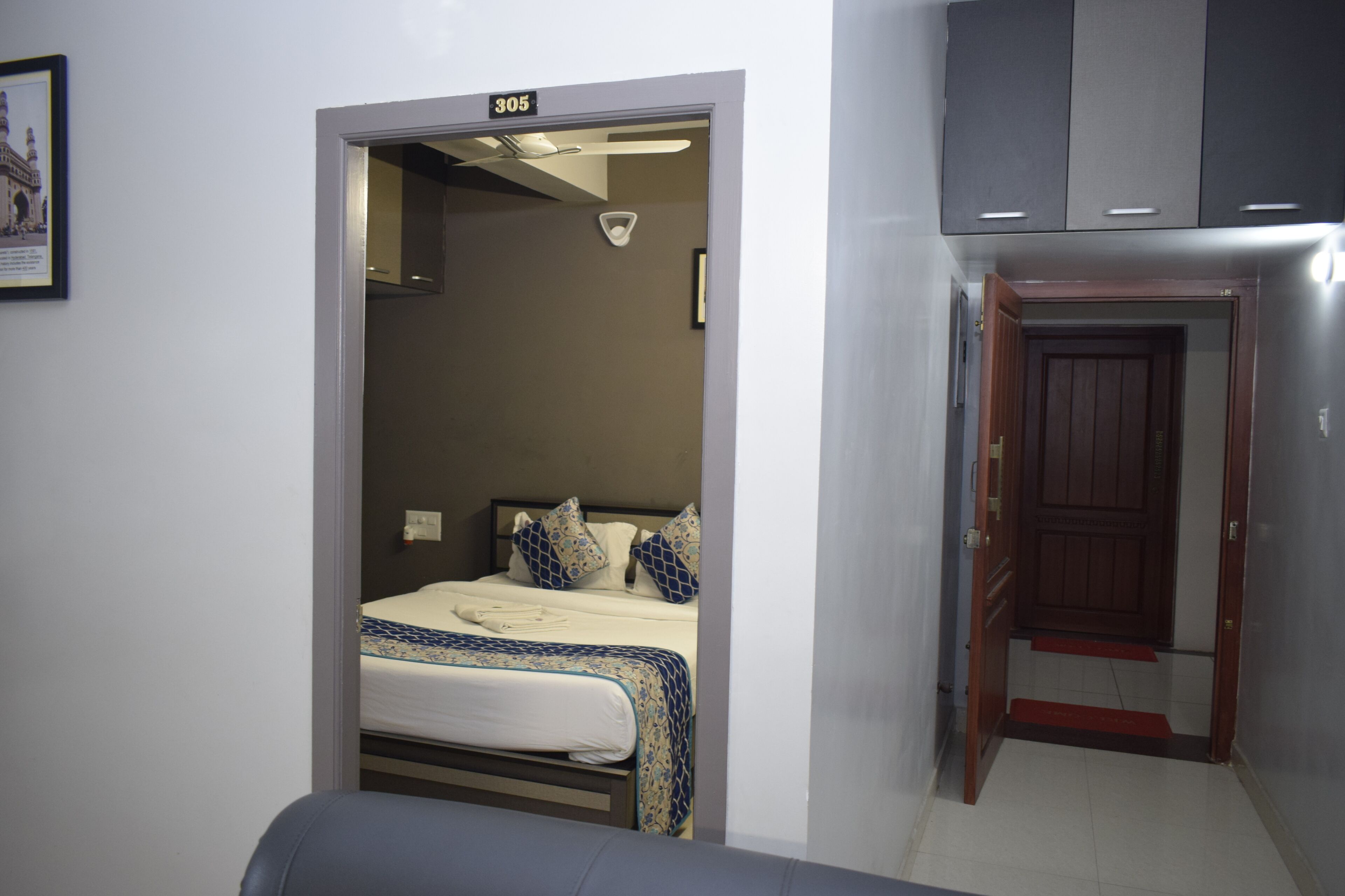 A hotel room with a bed, a door, and a wall-mounted light fixture.