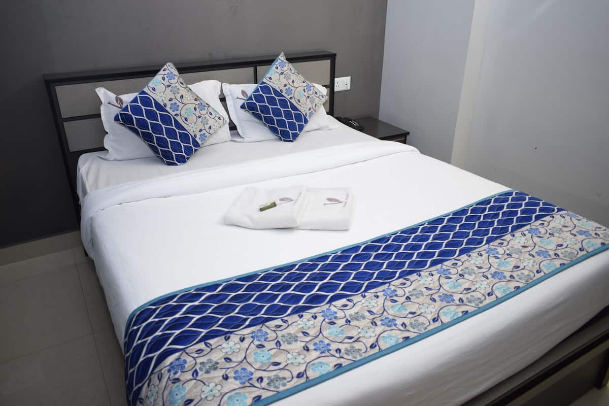 Uma cama bem arrumada com um cobre-leito azul e branco estampado, duas almofadas com um padrão geométrico azul e um controle remoto sobre uma mesa de cabeceira.