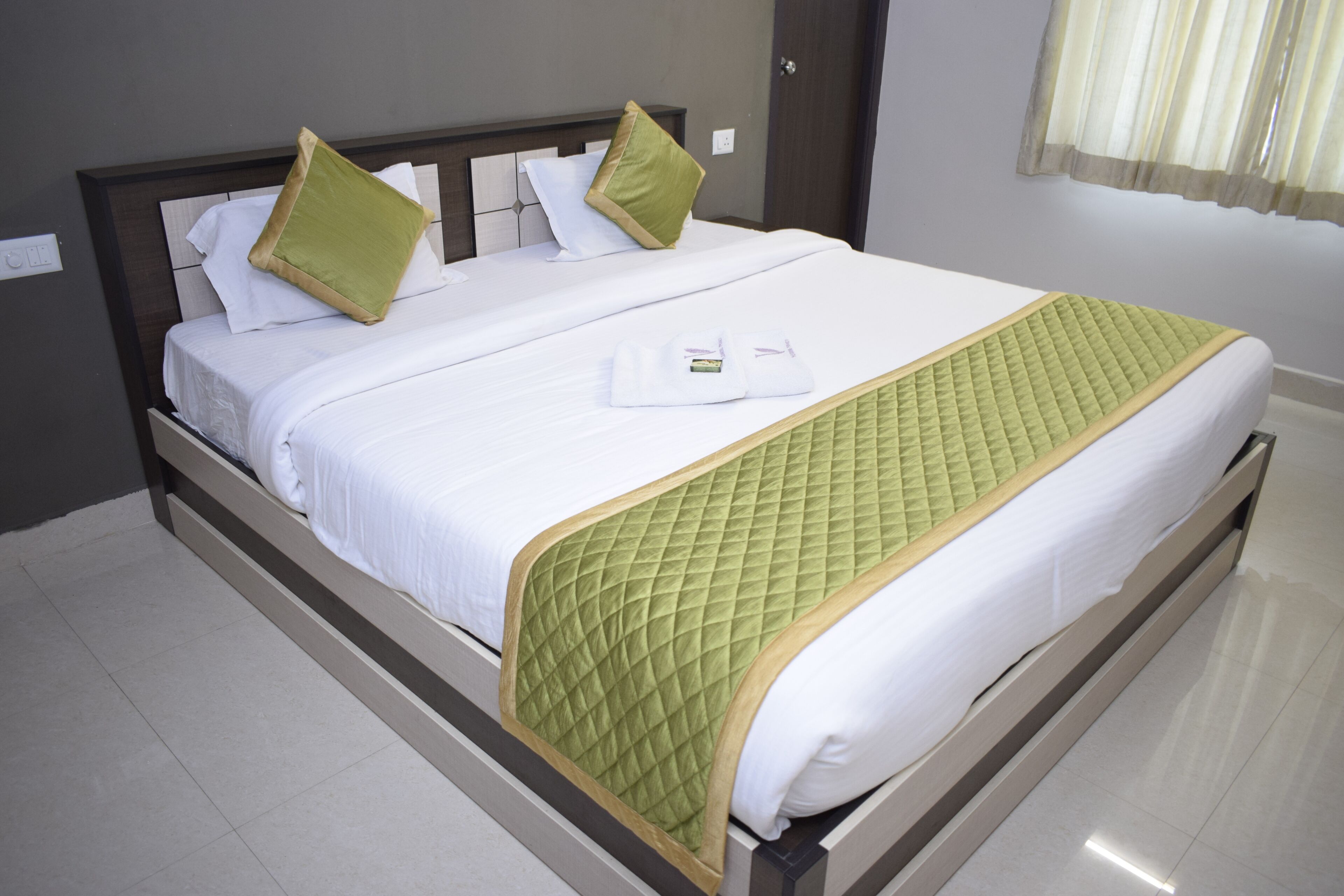 A neatly made bed with a quilted green blanket and white linens, a wooden headboard, and a white pillow with a green accent.