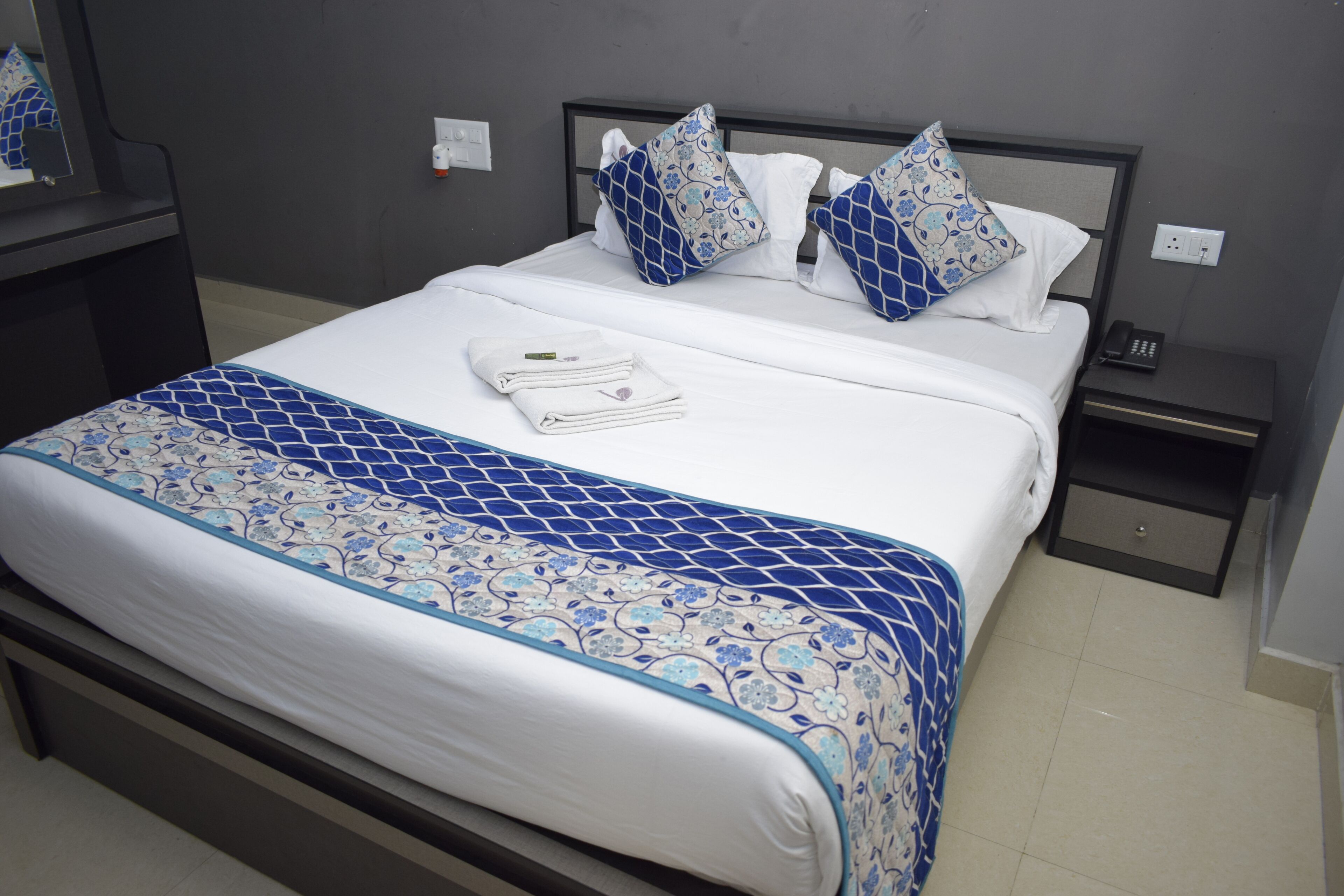 A neatly made bed with a patterned bedspread, a bedside table with a phone, and a mirror on the wall.