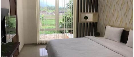 Quarto de hotel com uma cama grande, televisão sobre um suporte, parede decorativa e vista para uma paisagem verde pela janela.