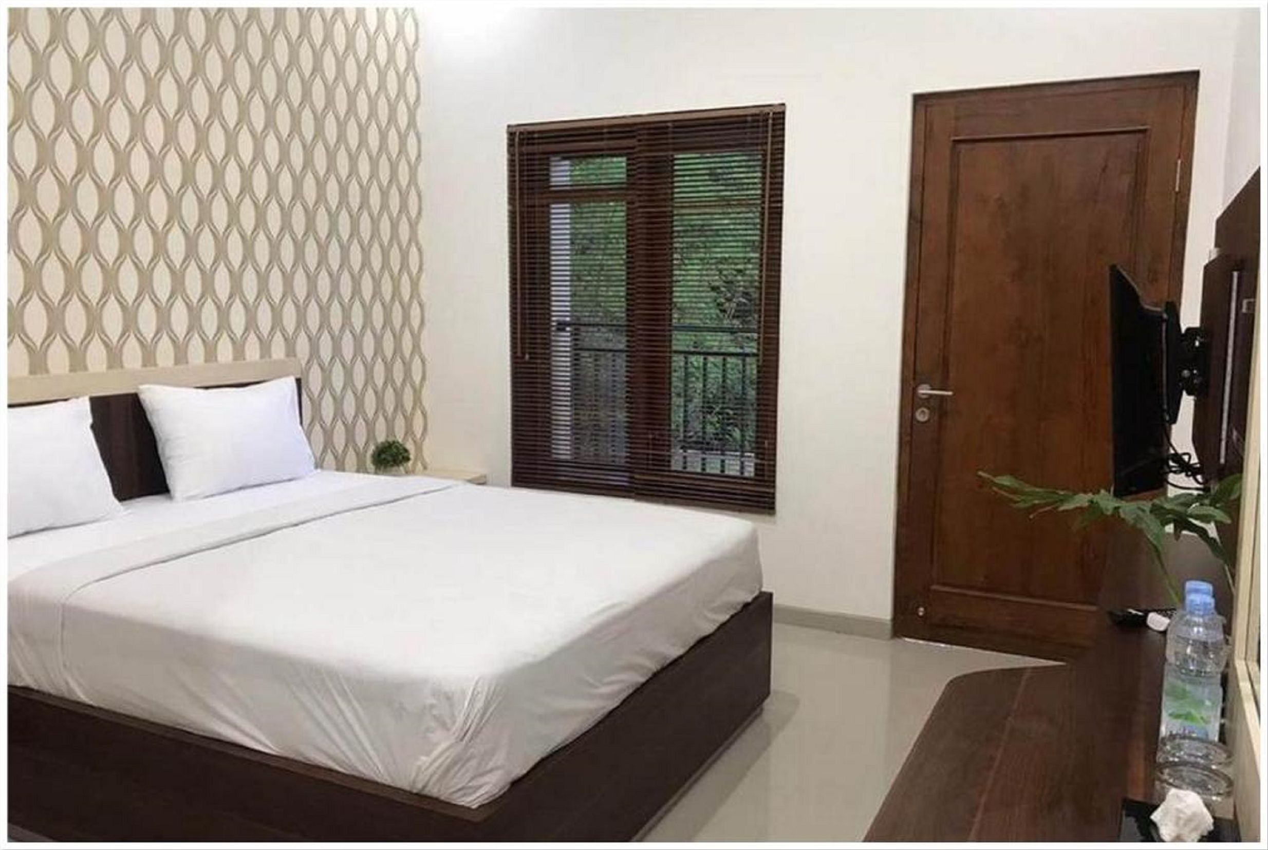 A bedroom with a bed, a wooden door, a window with blinds, and a wall with a geometric pattern.