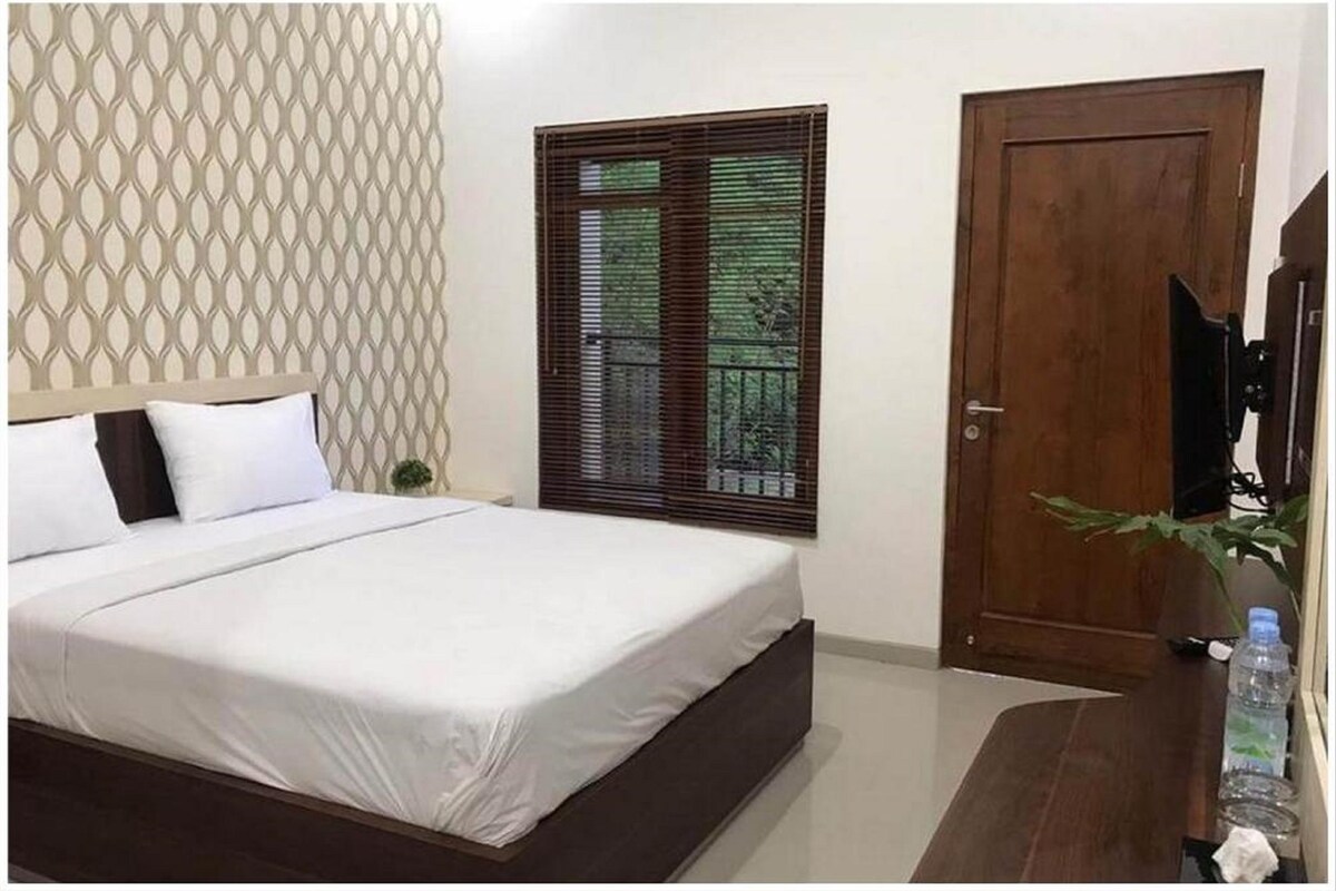 A bedroom with a bed, a wooden door, a window with blinds, and a wall with a geometric pattern.