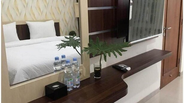 Habitación de hotel con cama, televisor, planta y una mesita con botellas de agua y un vaso.