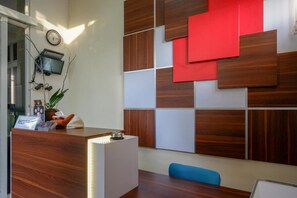 A reception area with a wooden reception desk, a clock, and a wall with a geometric pattern. - Reddoorz Syariah @ Omah Sawah (Ngaglik)