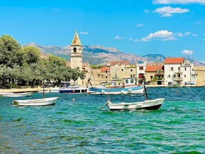 A coastal town with boats docked along the waterfront, a prominent tower, and buildings with red roofs.