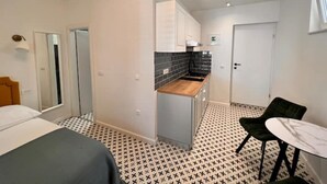A compact hotel room with a bed, a small kitchenette, a dining area with a table and chairs, and a bathroom with a mirror and toilet. - Studio apartment by the sea (Kaštel Sućurac)