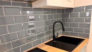 A modern kitchen with a black sink, wooden countertop, and grey tiled backsplash. - Studio apartment by the sea (Kaštel Sućurac)