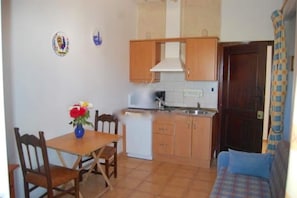 Une cuisine compacte avec des meubles en bois, un petit réfrigérateur et une table à manger avec des chaises.
