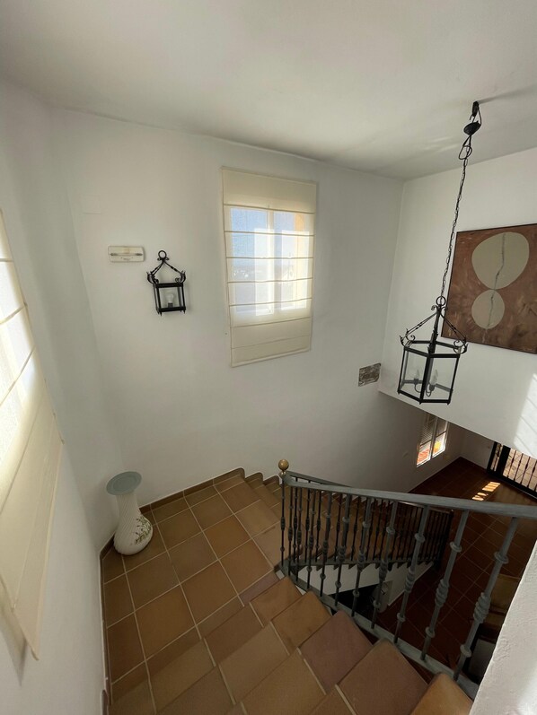 Una escalera con barandilla de metal, una ventana con persianas y un aplique en la pared.