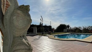 A swimming pool with a tiled deck, a stone sculpture, and a clear sky.