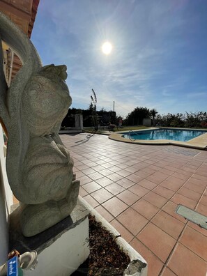 Una piscina con solana empavedada, una escultura de piedra y un cielo despejado.