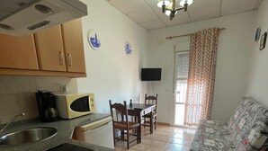 A compact kitchen with a microwave, stove, and sink, a dining area with chairs and a table, and a sofa in a living area.