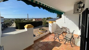 A balcony with a tiled floor, a chair, a table, and a view of the surrounding area.