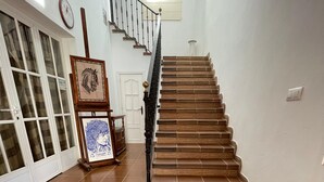 Una escalera con escalones de madera y barandal negro, que conduce a un rellano con una puerta blanca y un cuadro enmarcado.
