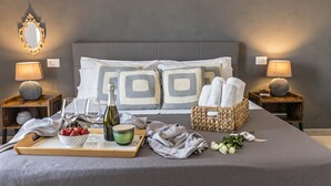 Una cama bien hecha con almohadas, una bandeja con fresas, una botella y una cesta de toallas.