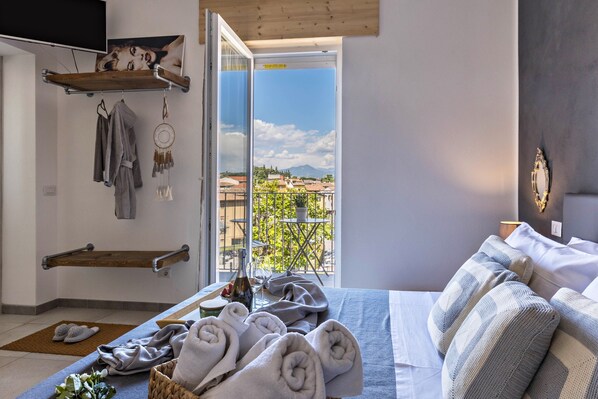 A bedroom with a bed, towels, a window with a view, and a shelf with items.