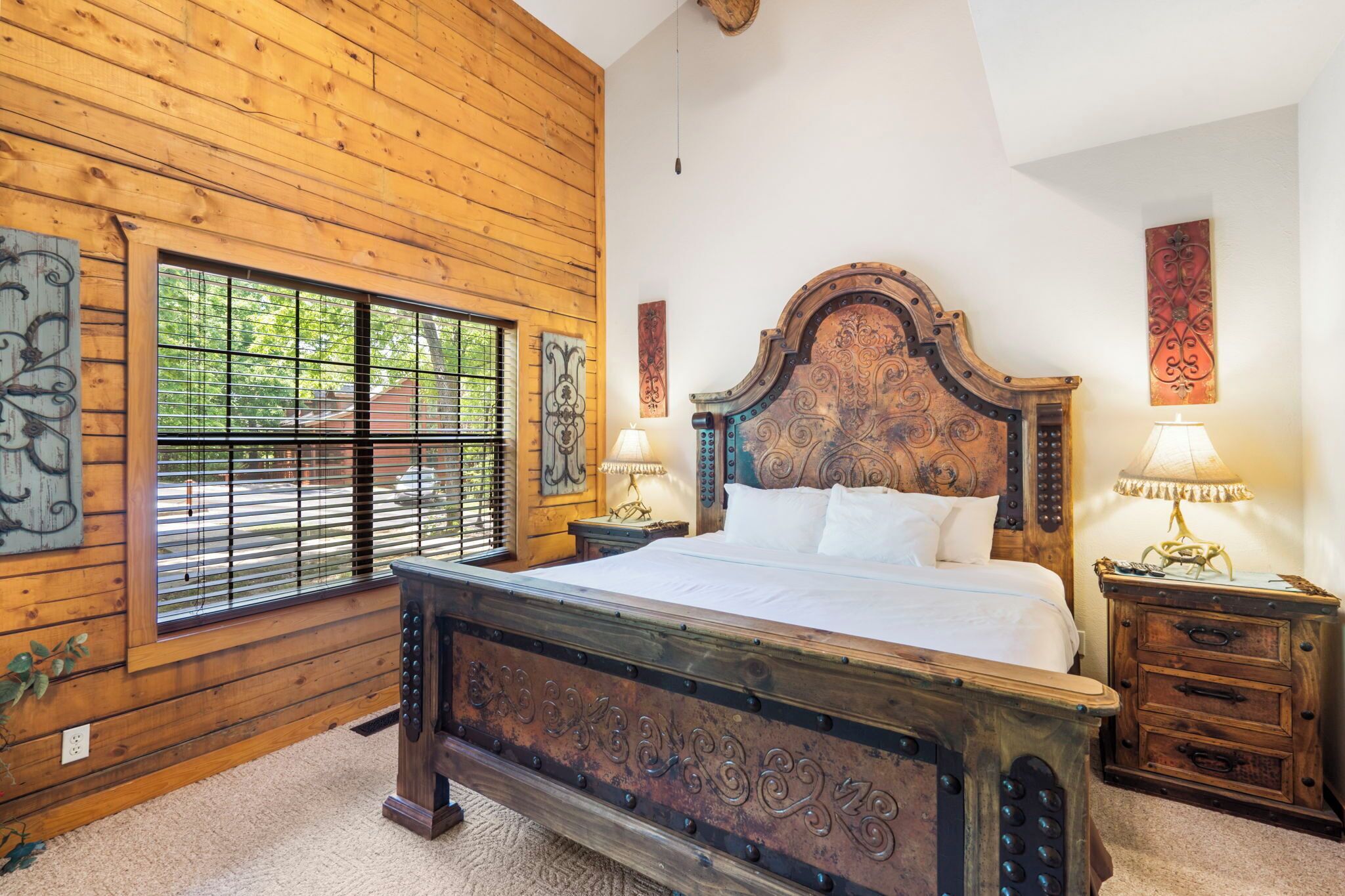 Une chambre à coucher aux murs lambrissés, avec un grand lit, deux tables de chevet dotées de lampes et des œuvres d’art décoratives.