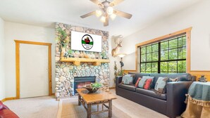 Una sala de estar acogedora con chimenea de piedra, un sofá, una mesa de centro y un ventanal con vistas a la vegetación.