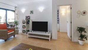 Una sala de estar con televisor de pantalla plana, un sofá, una mesa de centro y una planta en maceta.
