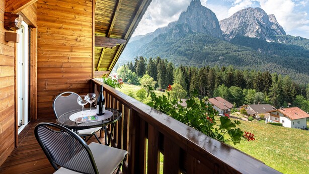 Ein Holzbalkon mit Tisch und Stühlen, mit Blick auf eine gebirgige Landschaft mit Häusern.