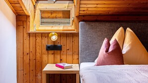 Ein kleines Zimmer mit einem Bett, einem Nachttisch, einem Fenster und einer Wandlampe.