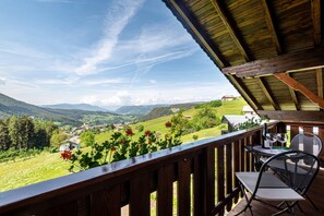 Une terrasse en bois avec une table et des chaises, donnant sur une vallée parsemée de maisons et de verdure.