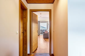 Un couloir mène à un espace de vie comprenant un canapé et offrant une vue sur l’extérieur.
