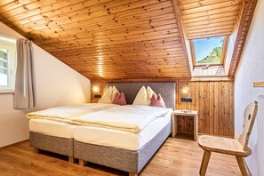 Quarto com teto de madeira, cama com almofadas, mesa de cabeceira e uma cadeira.