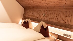 A bedroom with a sloped ceiling, wooden paneling, a bed with pillows, and a bedside table with a power outlet.