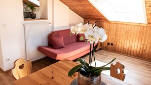 A cozy room with a sloped ceiling, a wooden table, a red sofa, and white orchids.