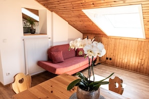 Une pièce chaleureuse avec un plafond en pente, une table en bois, un canapé rouge et des orchidées blanches.
