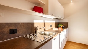 Una cocina moderna con un lavamanos de acero inoxidable, armarios blancos y un electrodoméstico rojo sobre la encimera.
