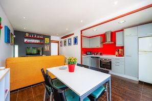 A modern kitchen with white cabinets, a red accent wall, and a dining area with a white table and chairs.