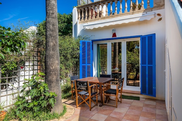A patio with a table and chairs, a white building with blue shutters, and a balcony with a railing.