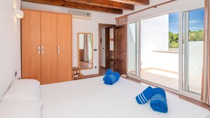 A bedroom with a large bed, wooden wardrobe, and a sliding glass door leading to a balcony.