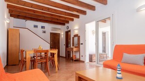 A living room with a wooden table, orange sofa, wooden chairs, a staircase, and a dining area.