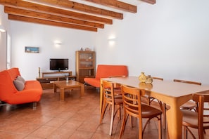Een woonkamer met een houten eettafel, een oranje bank en een televisie.