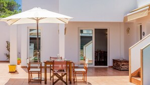 An outdoor patio with a table and chairs, a white umbrella, and a staircase leading to an upper level.