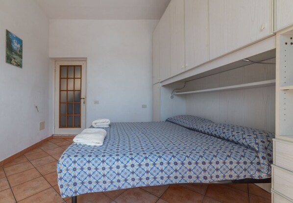 Una habitación pequeña con una cama, una puerta y un armario blanco.