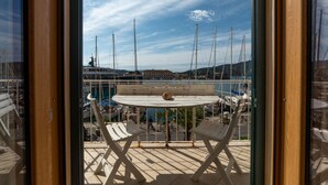 Un balcón con una mesa y sillas, con vista a un puerto deportivo con barcos y un pueblo a lo lejos.