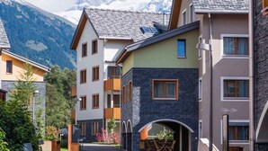 A modern hotel with a stone facade, multiple balconies, and a view of snow-capped mountains. - Holiday apartment with wellness area (Engelberg)