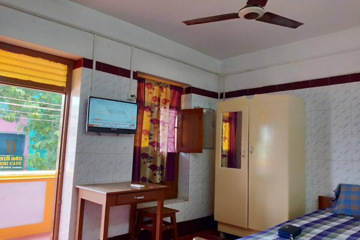 A room with a bed, a desk, a wardrobe, a television, and a window with a view of a building outside.