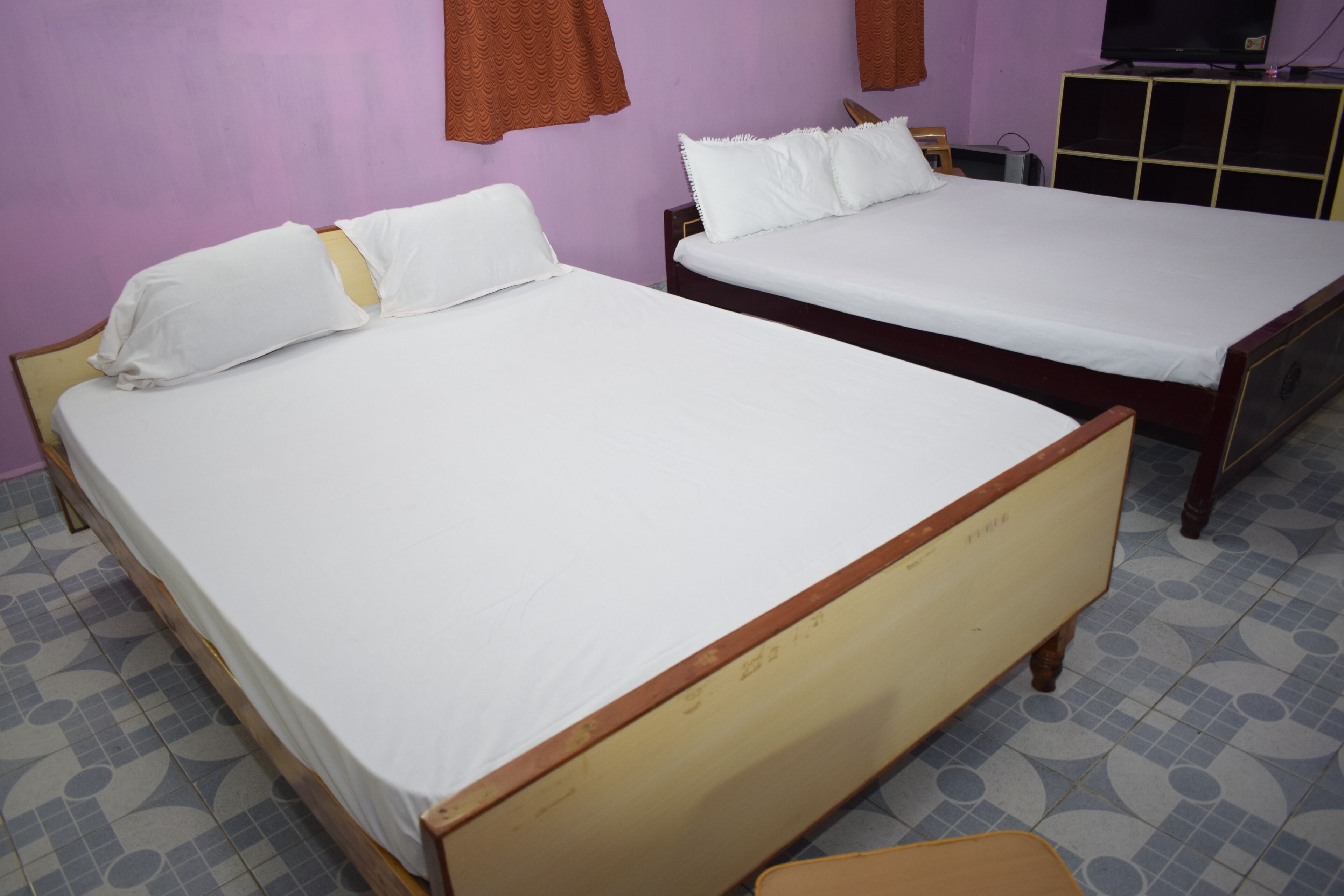 Two single beds with wooden frames and white bedding in a room with purple walls and patterned floor tiles.