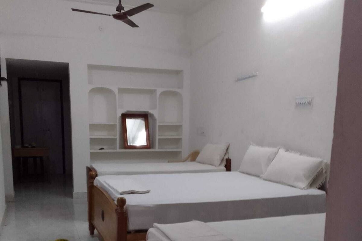 A room with two wooden beds, a ceiling fan, a small window, and a built-in shelf unit.