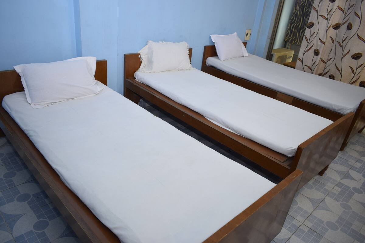 Three wooden single beds with white linens in a room with blue walls and patterned floor tiles.