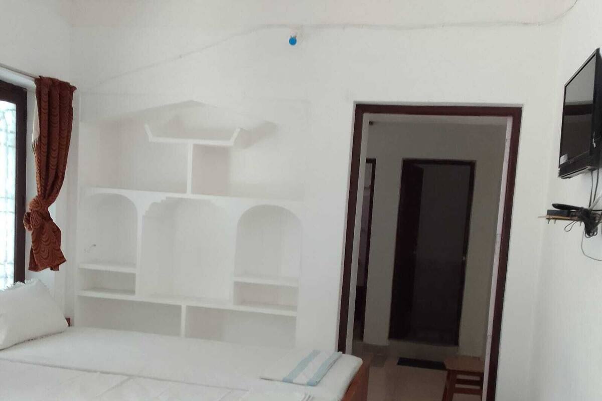 A bedroom with a bed, a desk, and a TV mounted on the wall.