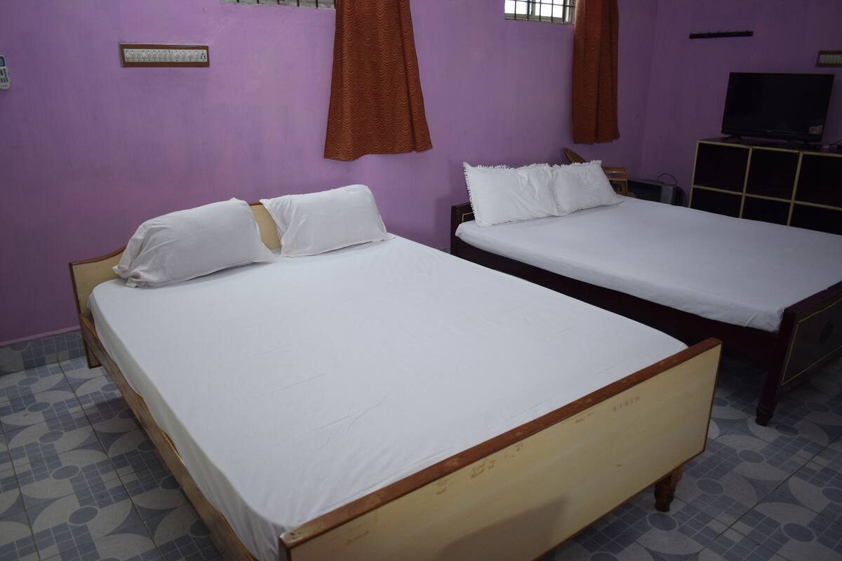 Two single beds with white linens in a room with purple walls and patterned floor tiles.